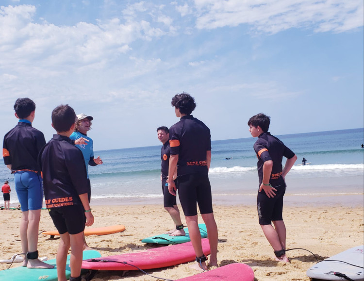 Raphael de Surf Guides explique le surf à un groupe de jeunes garçons sur la plage