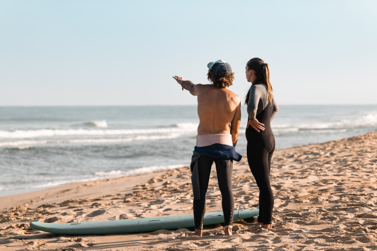 Raphael de Surf Guides montre l'océean à une surfeuse sur la plage